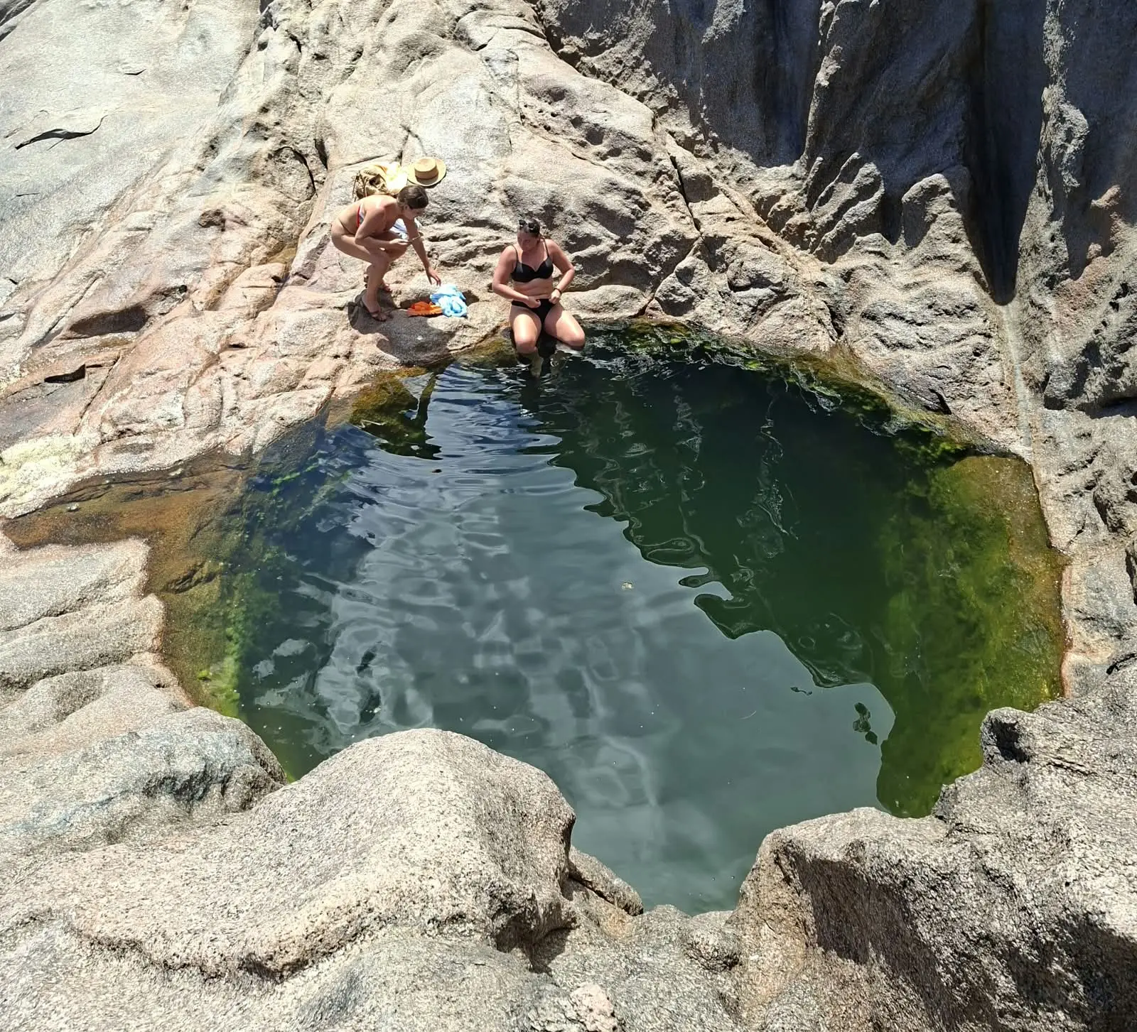 Natural tidal rock pool at Anse Takamaka with clear green water surrounded by granite boulders